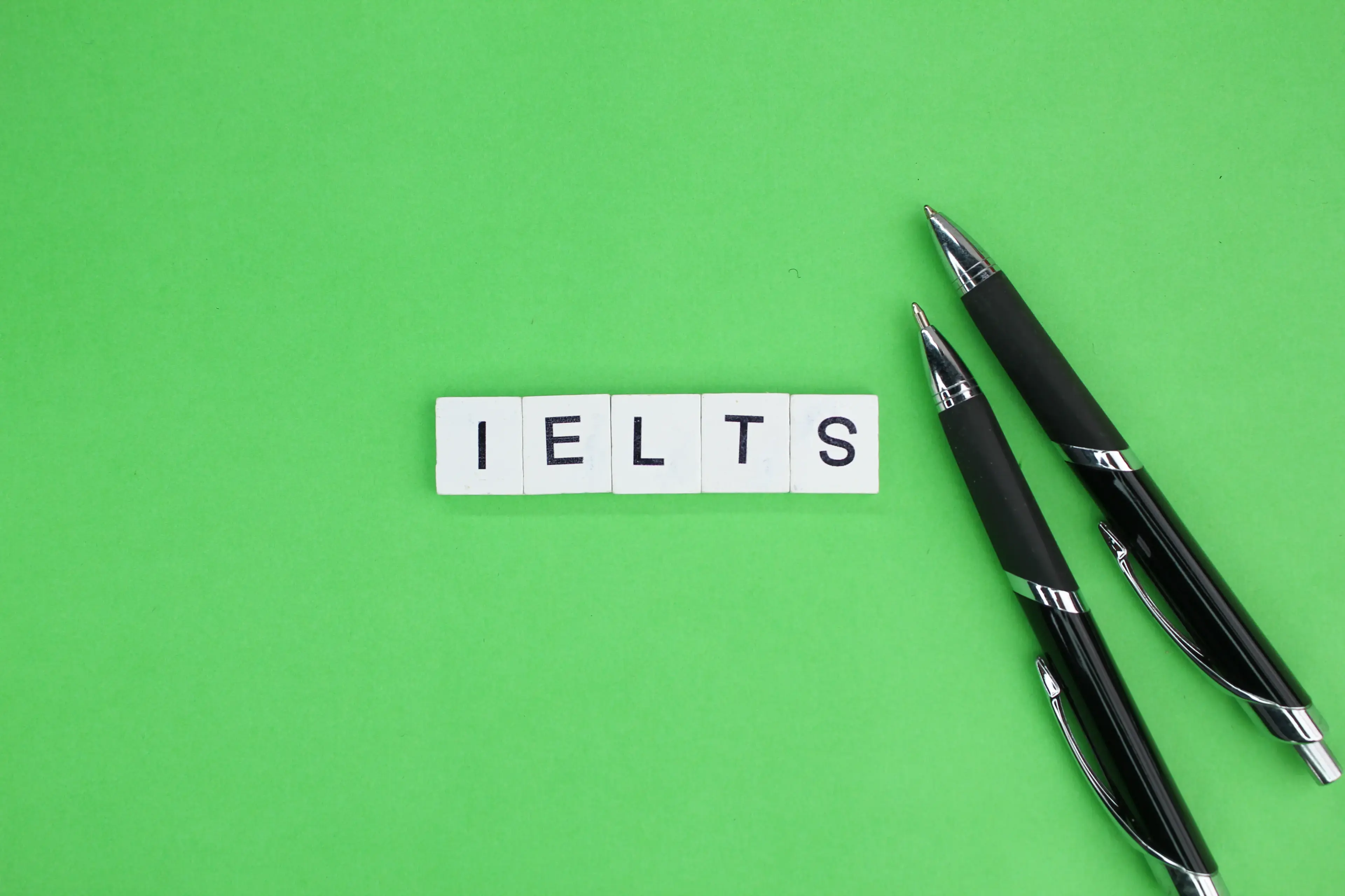 Yeşil zemin üzerinde IELTS yazan harf blokları ve yanlarında duran kalemler