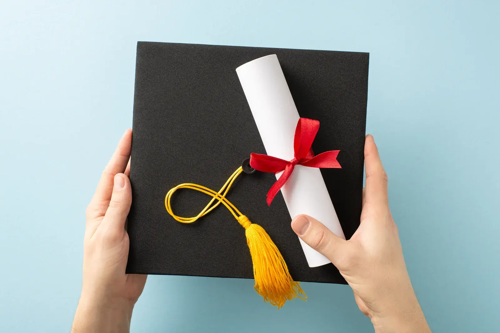 Mezuniyet keppini ve kırmızı kurdeleli diplomasını iki eliyle tutan mezun